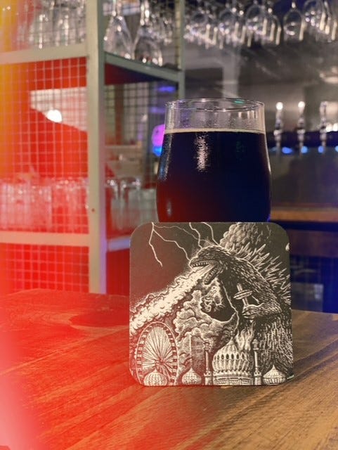 Image of a glass of stout behind a beer mat showing an image of Godzilla