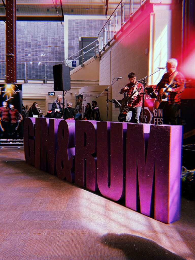 Image a two musicians behind large sign spelling Gin & Rum